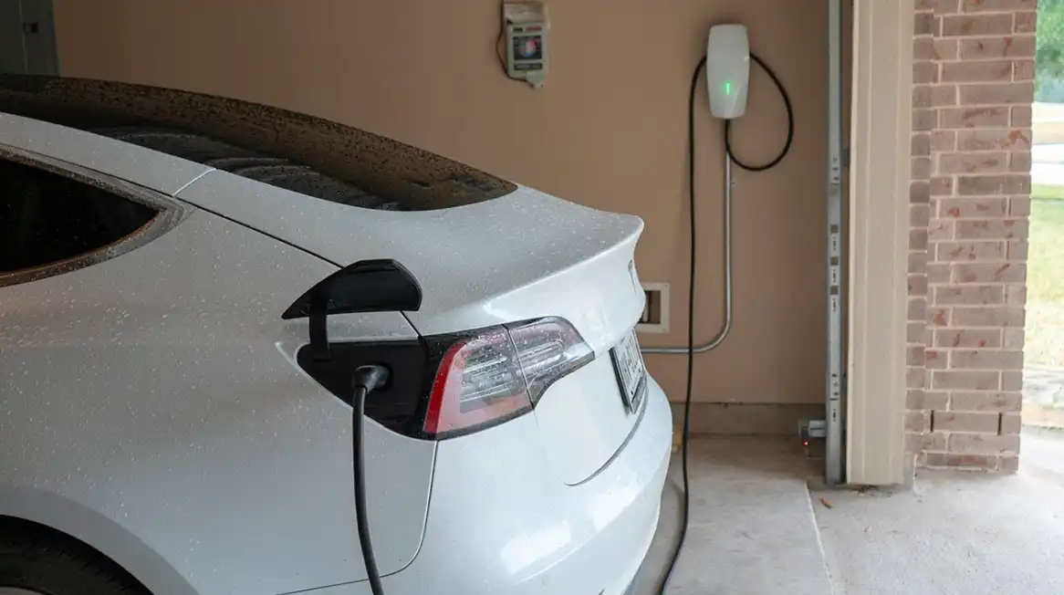 A white tesla electric vehicle parked in a garage connected to a charger